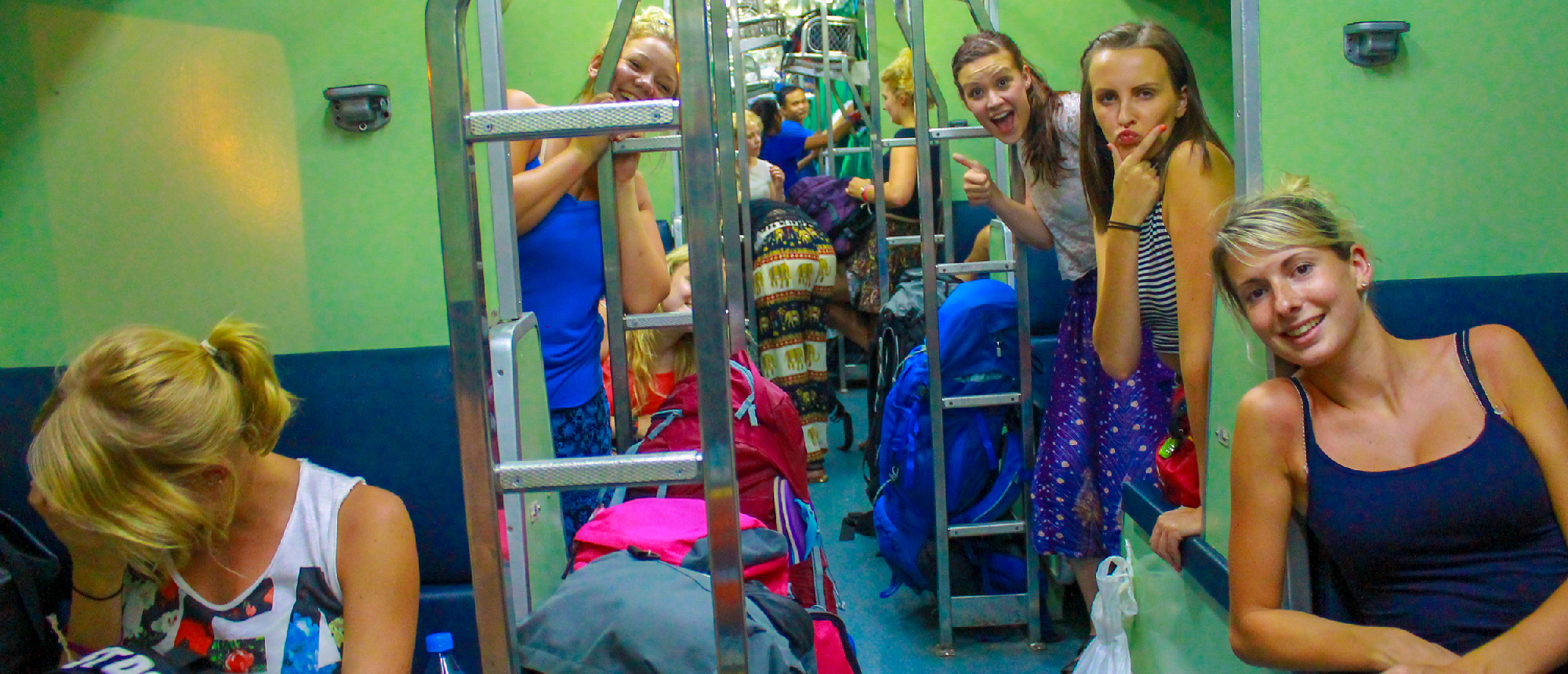Young women smile and pose in a vibrant overnight train carriage during their Thailand adventure.