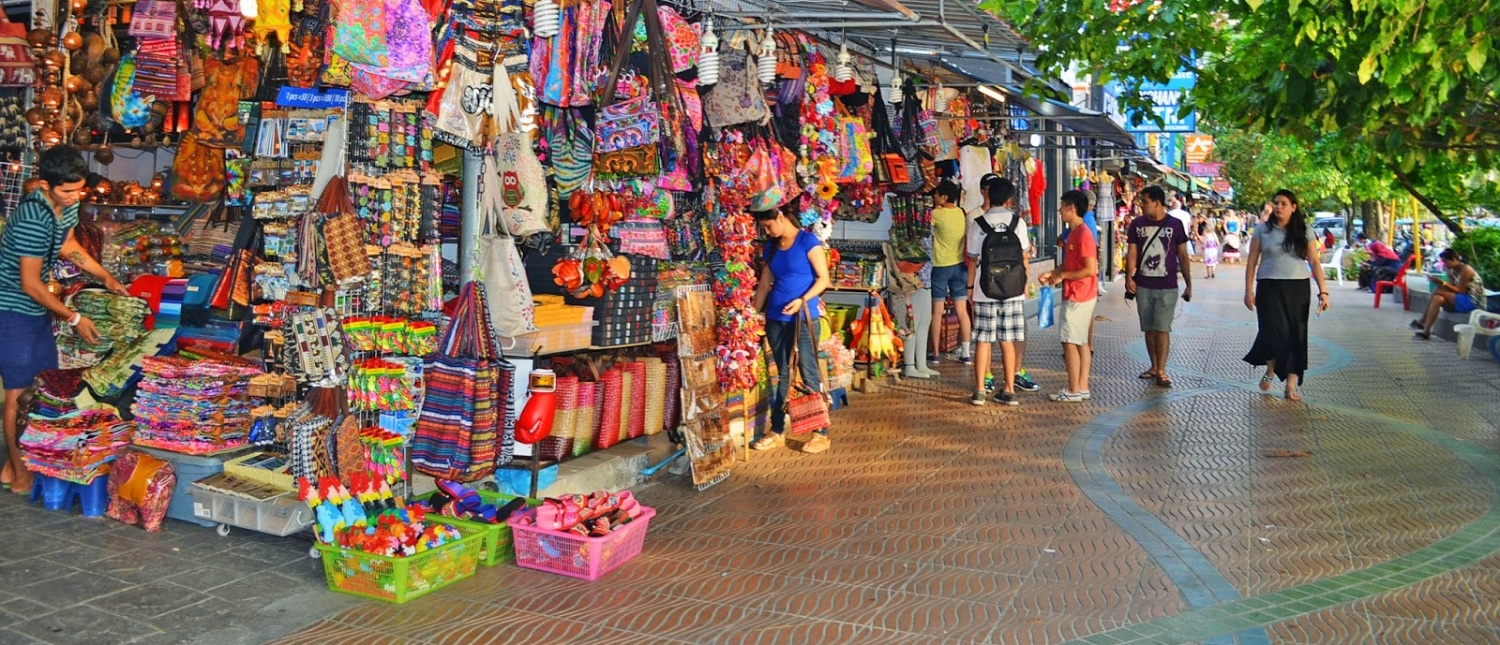 People browse colorful market stalls selling bags and souvenirs on a lively street in Krabi.