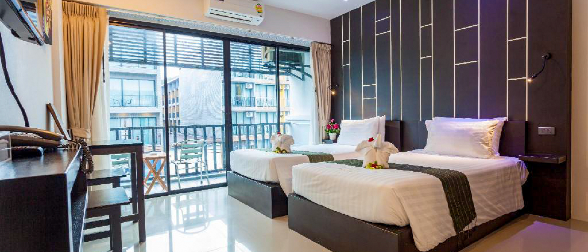 A modern hotel room with two neatly made twin beds, towel swans, and a balcony in Thailand.