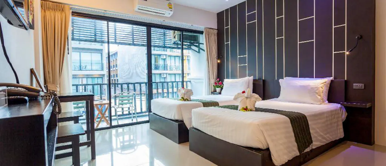 A bright, modern hotel room in Krabi with two comfortable beds, towel art, and a balcony.