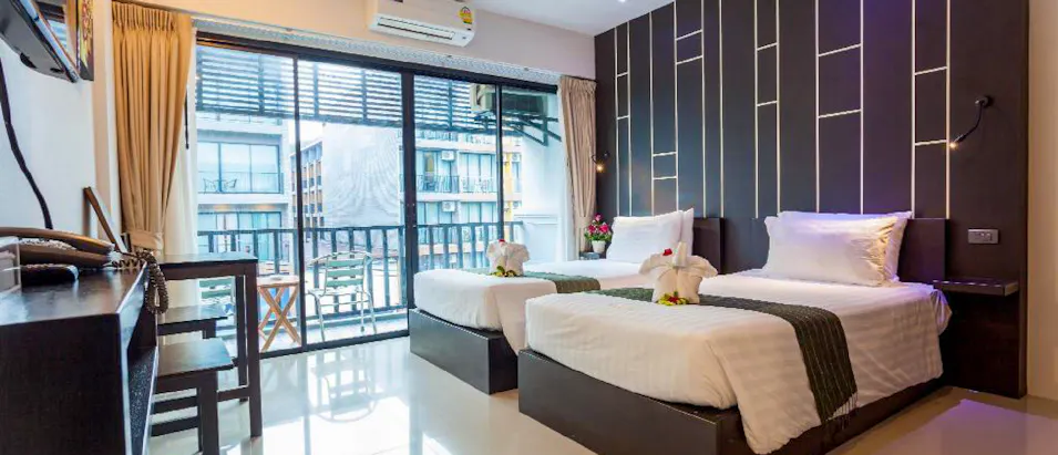A modern hotel room with two neatly made twin beds, towel swans, and a balcony in Thailand.