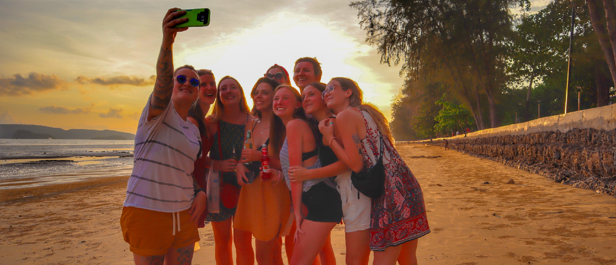 A group of happy young women taking a selfie on a sandy beach at sunset in Krabi.