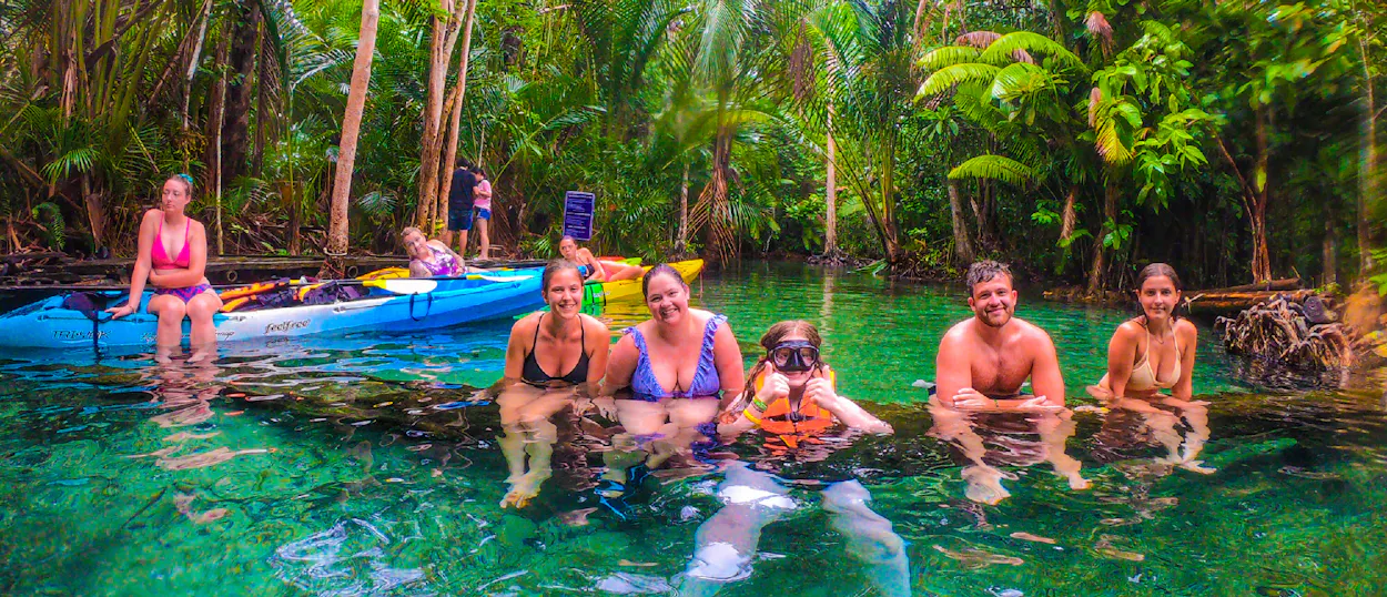 Happy friends and a child swim in the clear emerald river surrounded by lush jungle in Krabi.