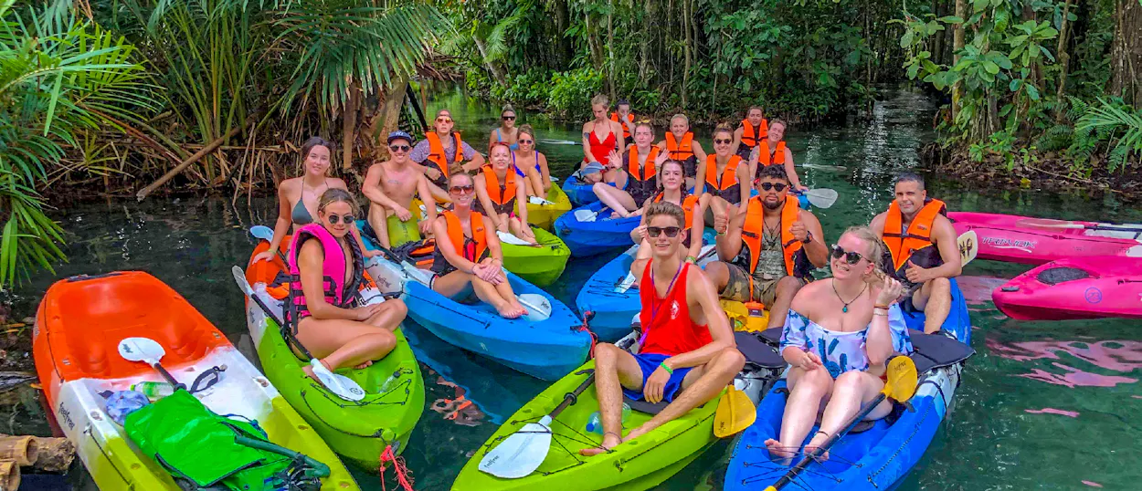 A group of happy tourists in colorful kayaks on clear emerald water in a Krabi mangrove.