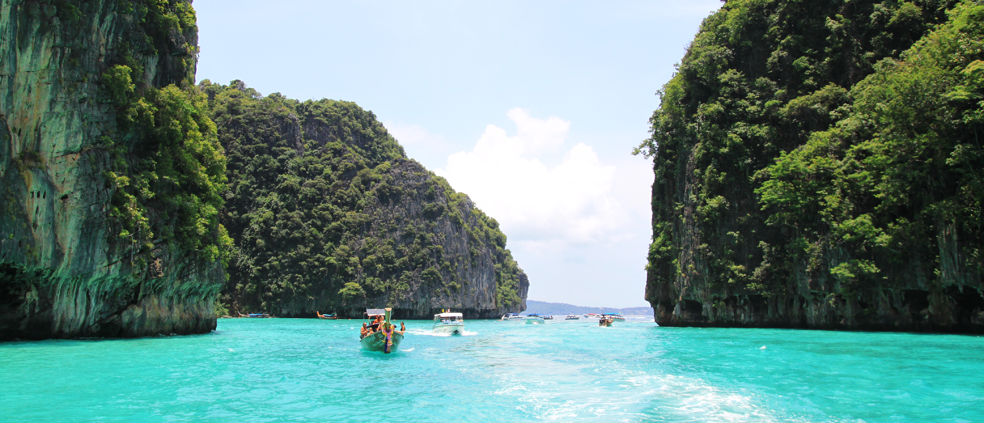 A longtail boat carries tourists through turquoise water between towering limestone cliffs in Koh Phi Phi.