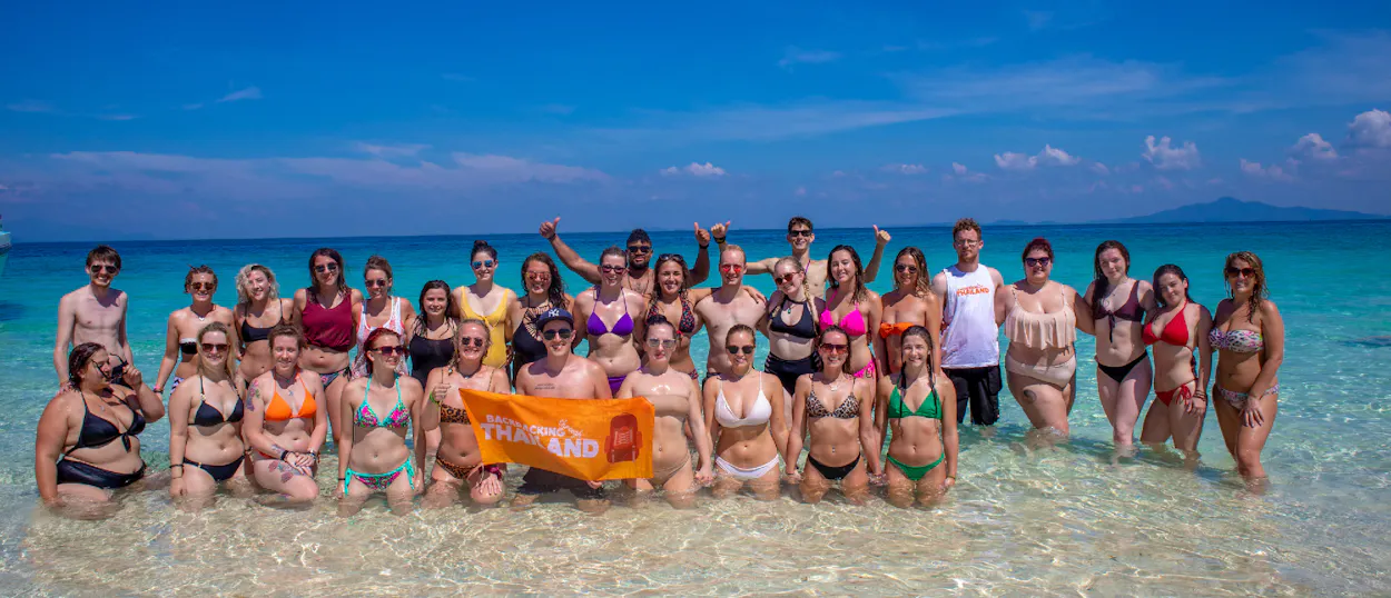 A large group of happy travelers pose in the clear turquoise waters of Koh Phi Phi, Thailand.