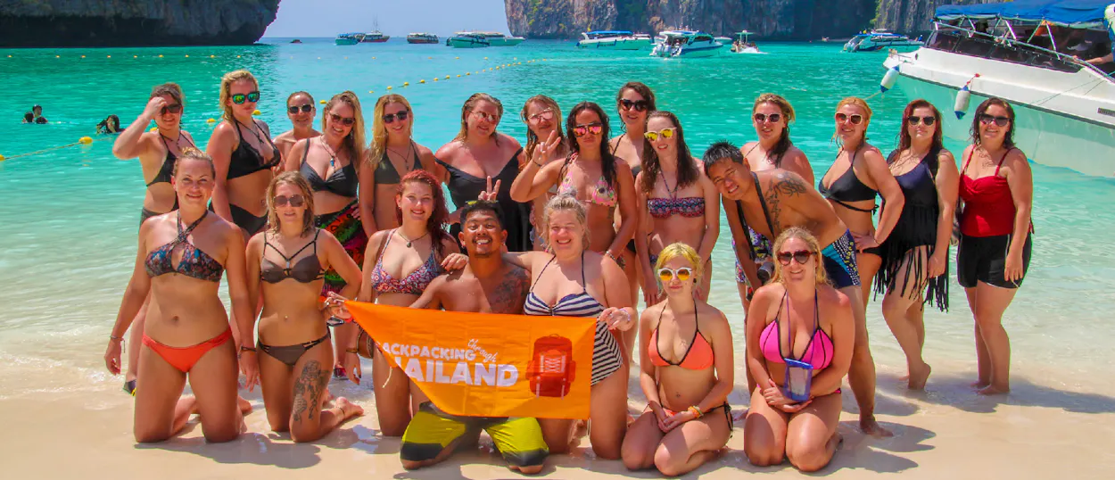 A happy group of backpackers posing on the sandy beach of Koh Phi Phi, Thailand.