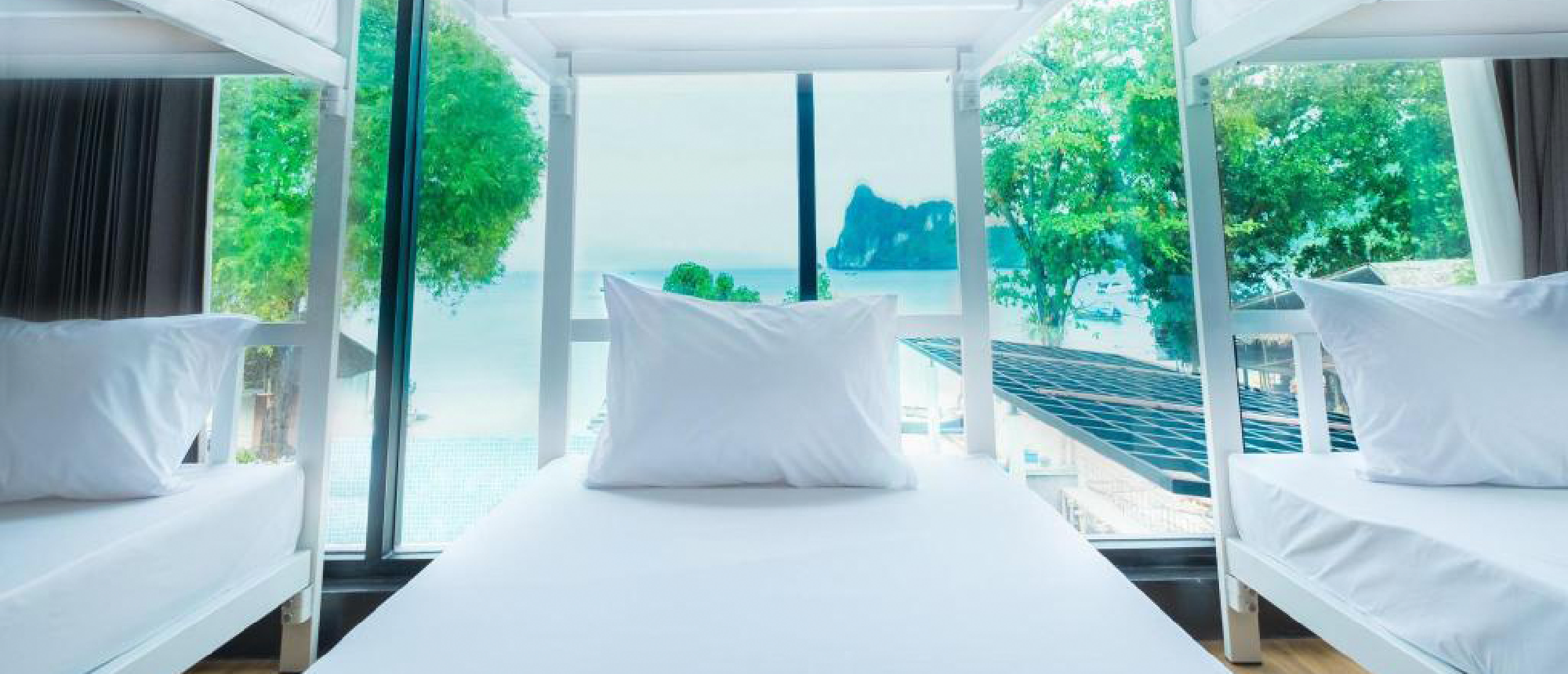 Clean hostel bunk beds with a panoramic view of a beautiful tropical bay in Thailand.