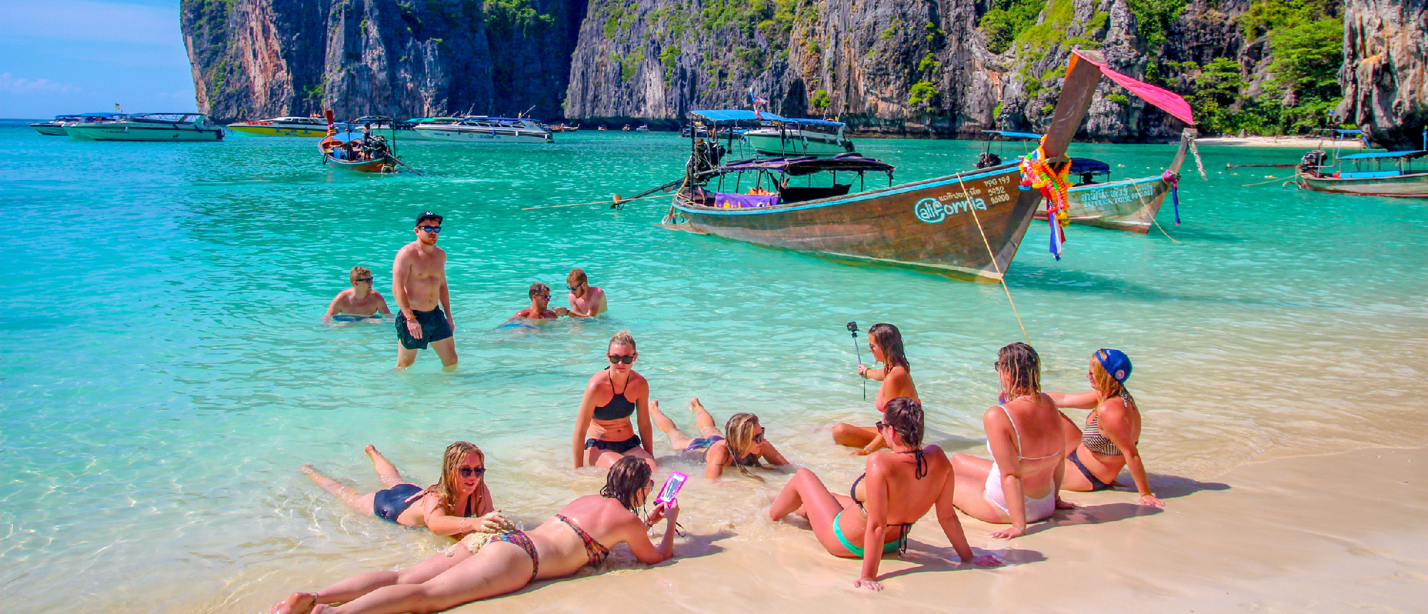 Backpackers relax on a stunning beach with turquoise water and limestone cliffs in Thailand's Phi Phi Islands.