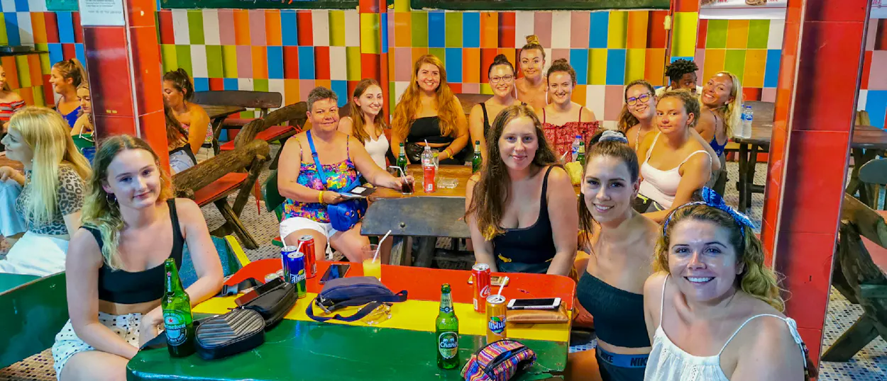 A group of smiling women enjoy drinks at a colorful bar in Thailand.