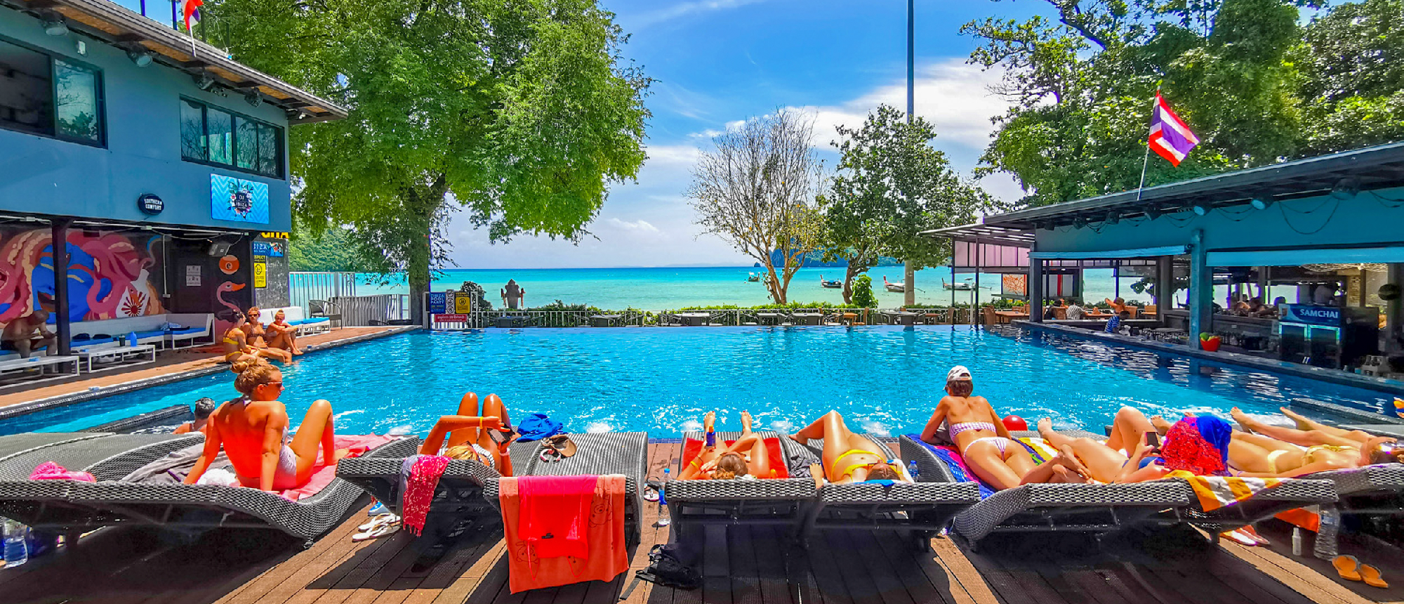 People sunbathe on loungers beside a resort pool with a stunning ocean view in Koh Phi Phi.