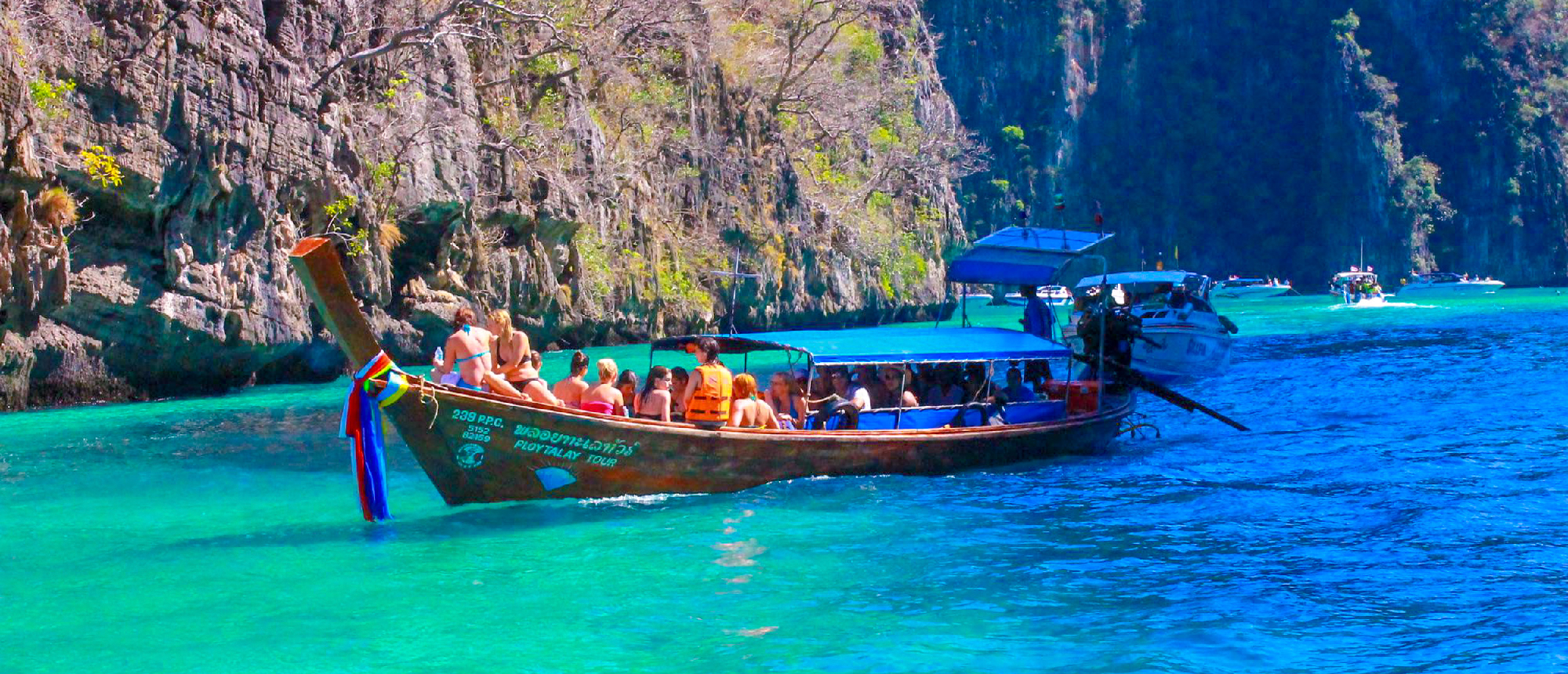 Tourists on a longtail boat navigate the turquoise waters near stunning limestone cliffs in Krabi, Thailand.