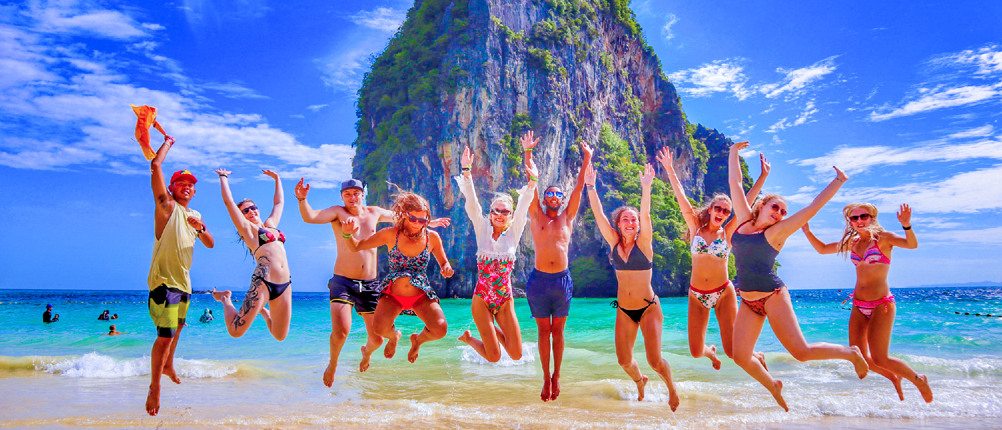 Joyful friends jump on white sands of Railay Beach, Krabi, against stunning limestone cliffs.