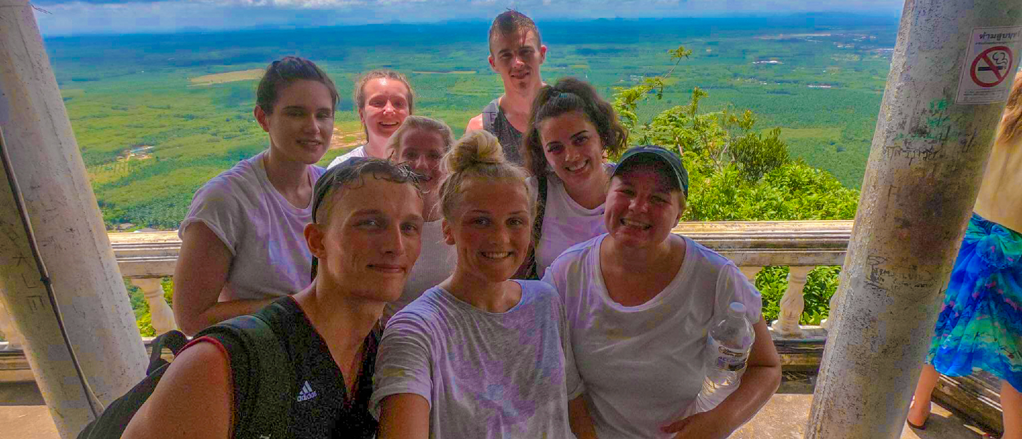 A group of happy hikers posing at the summit of Tiger Cave Temple with a scenic jungle view.