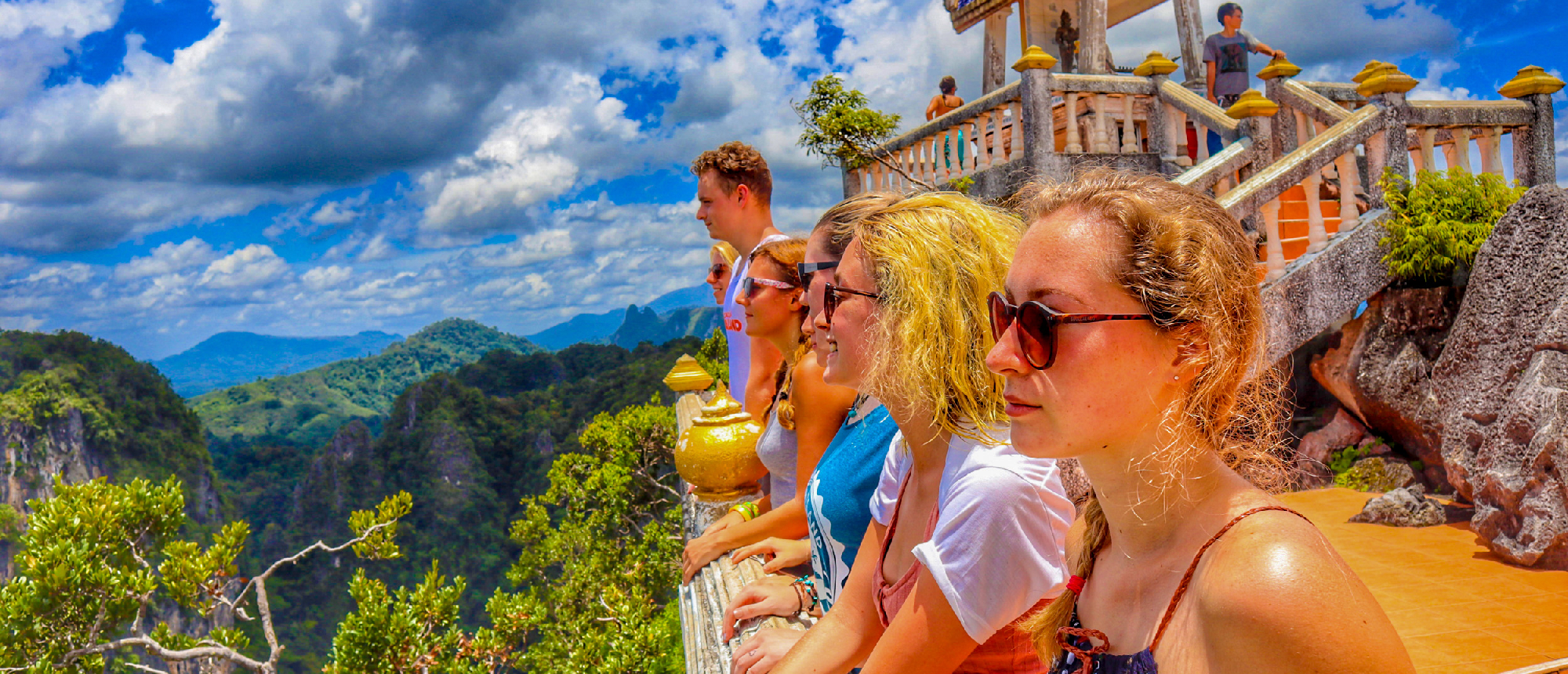 Backpackers admire the expansive green mountain landscape from a temple viewpoint in Krabi, Thailand.