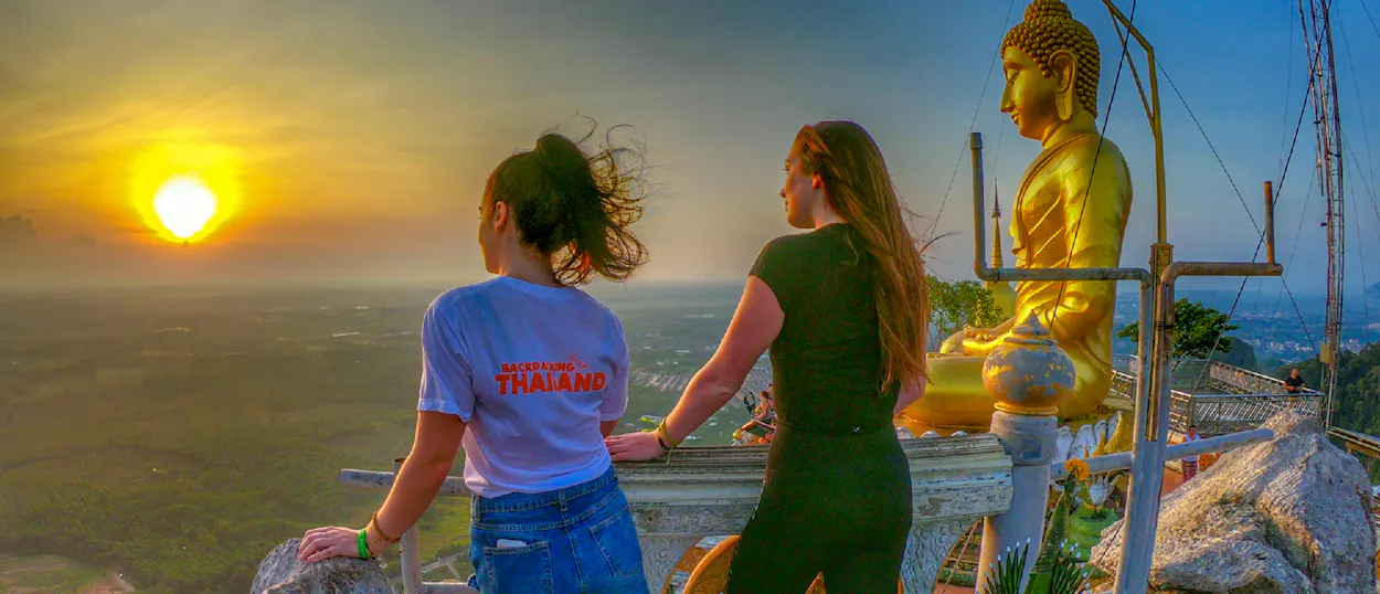 Two women watch a golden sunset over the Krabi landscape from a high temple viewpoint.