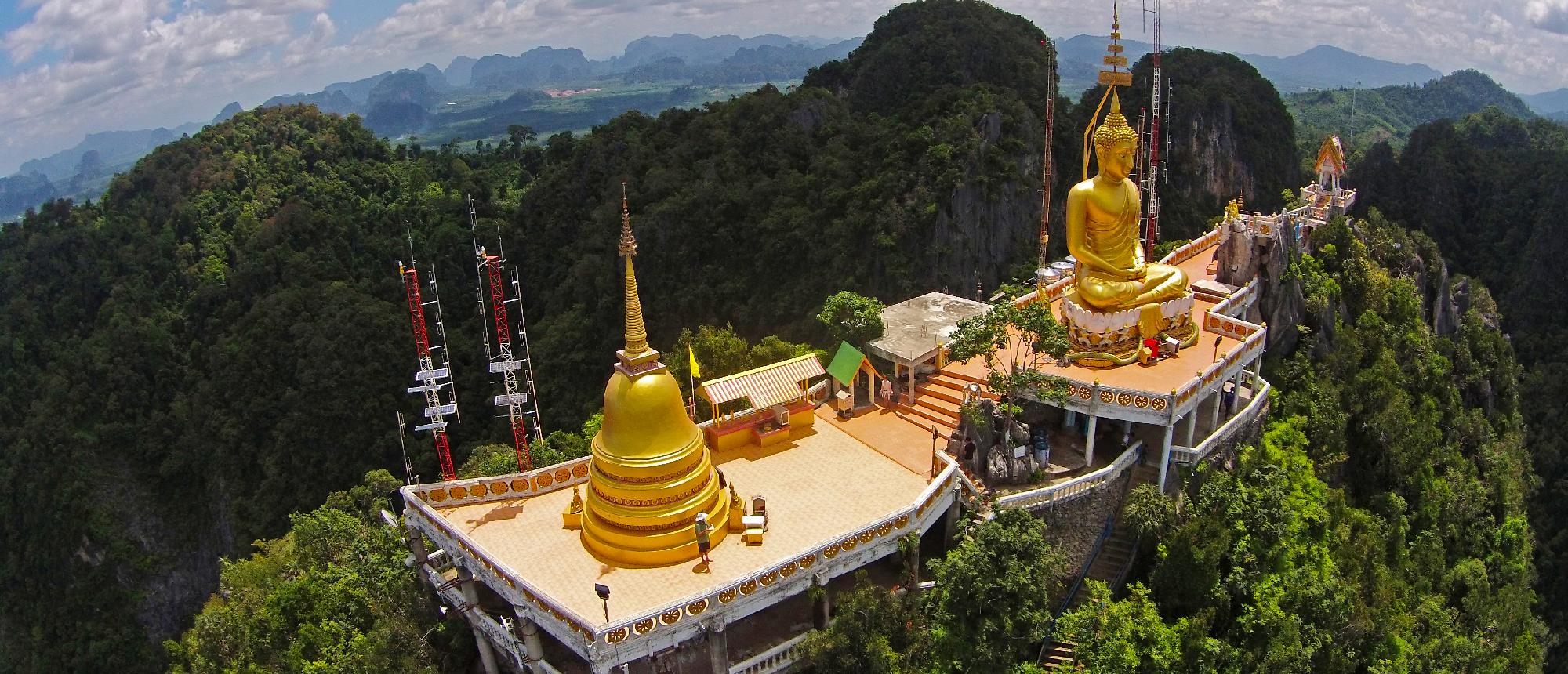 A golden Buddha statue and pagoda overlook lush mountains from a temple summit in Krabi.