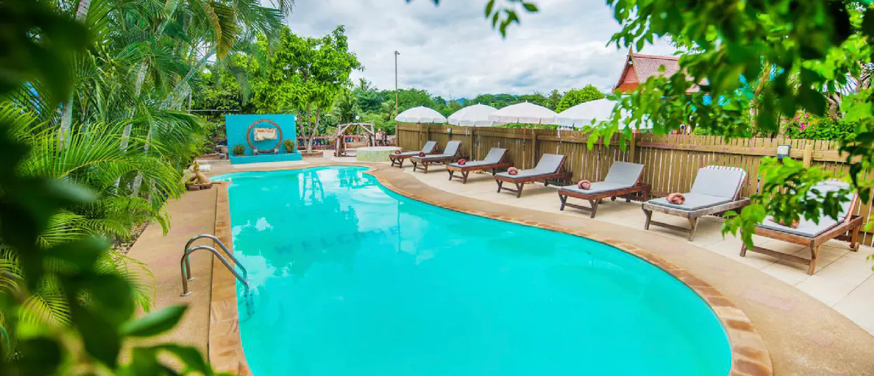 Inviting resort swimming pool with empty lounge chairs nestled among vibrant tropical foliage.