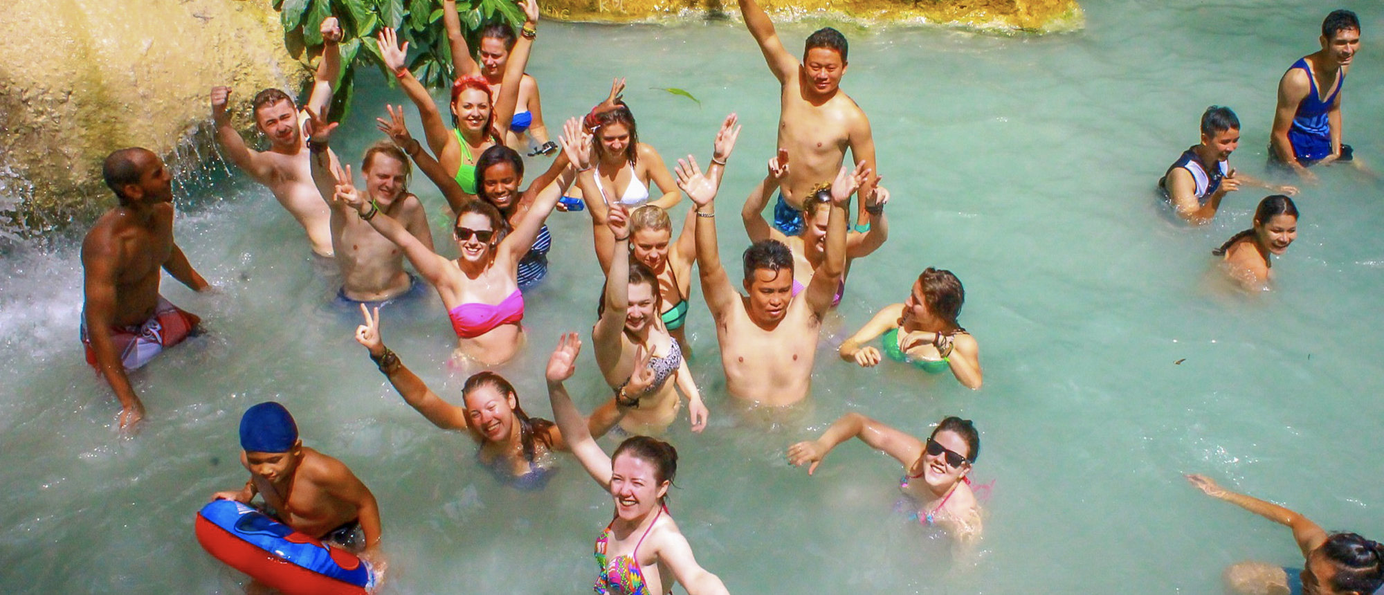 Joyful group of travelers swimming and waving in the emerald waters of Erawan National Park.