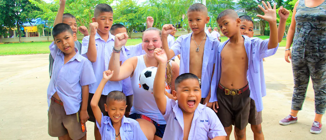 Happy Thai students and a guide cheer with a soccer ball at a school in Amaphawa.