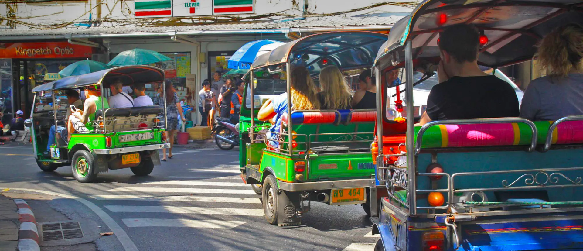 Travellers riding colourful tuk-tuks along a busy street in Bangkok
