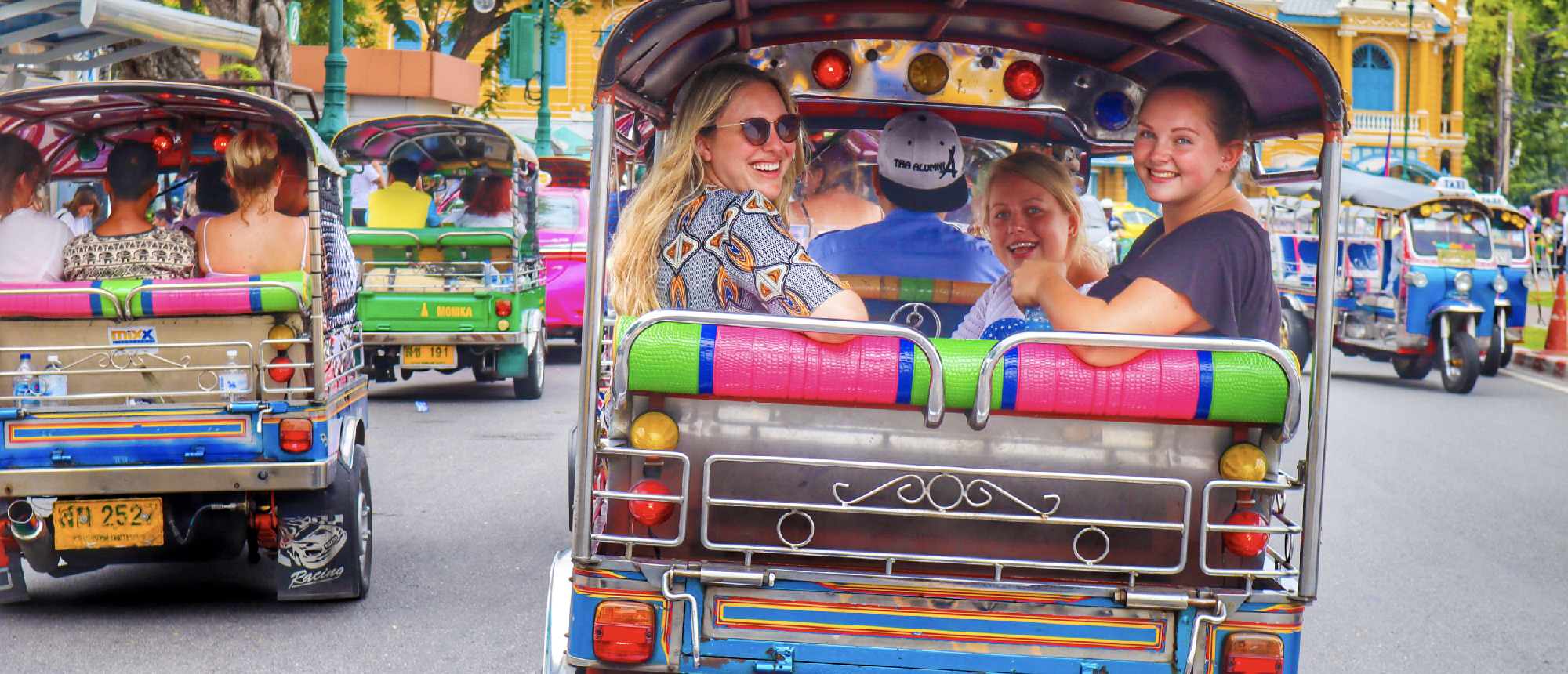 Smiling friends enjoy an exciting tuk-tuk ride through the vibrant city streets of Bangkok.