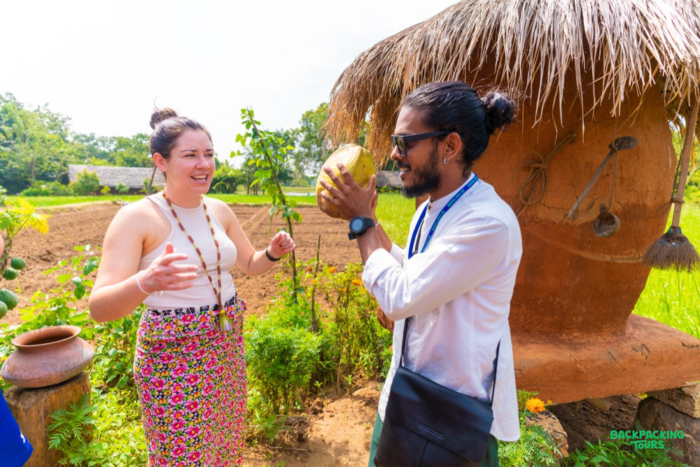 A woman and a man happily holding a coconut in a sunny, green field in Sri Lanka.