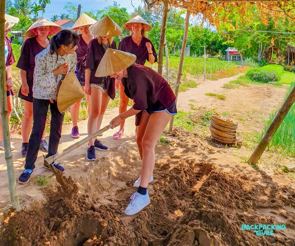Backpackers wearing conical hats learn to farm on a sunny day in Vietnam.