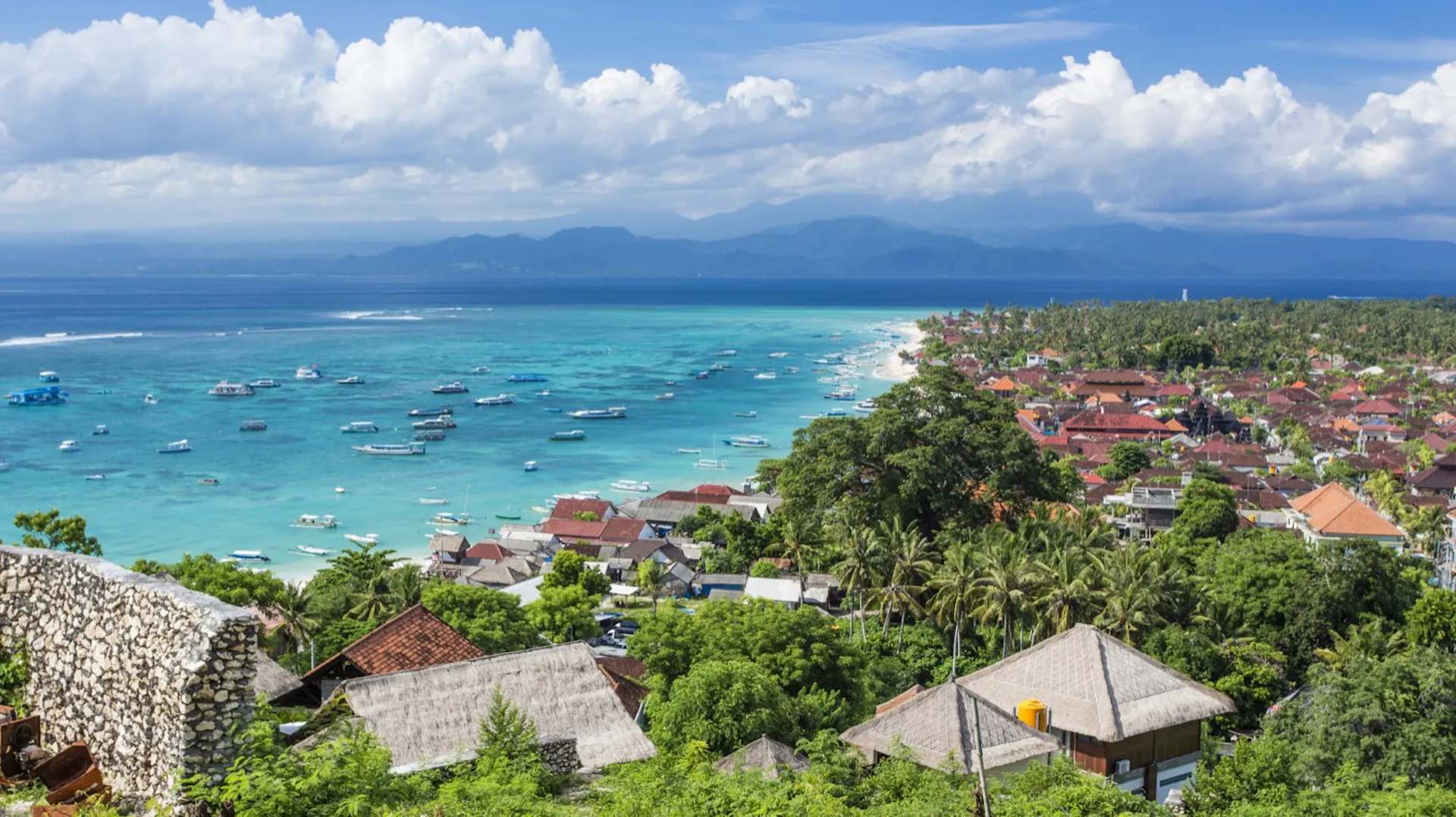 Beautiful coastal town with many boats in turquoise water and lush greenery, Bali.