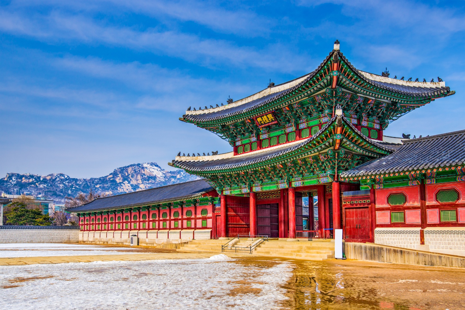 A vibrant Gyeongbokgung Palace in South Korea, featuring a snowy courtyard and majestic mountains.