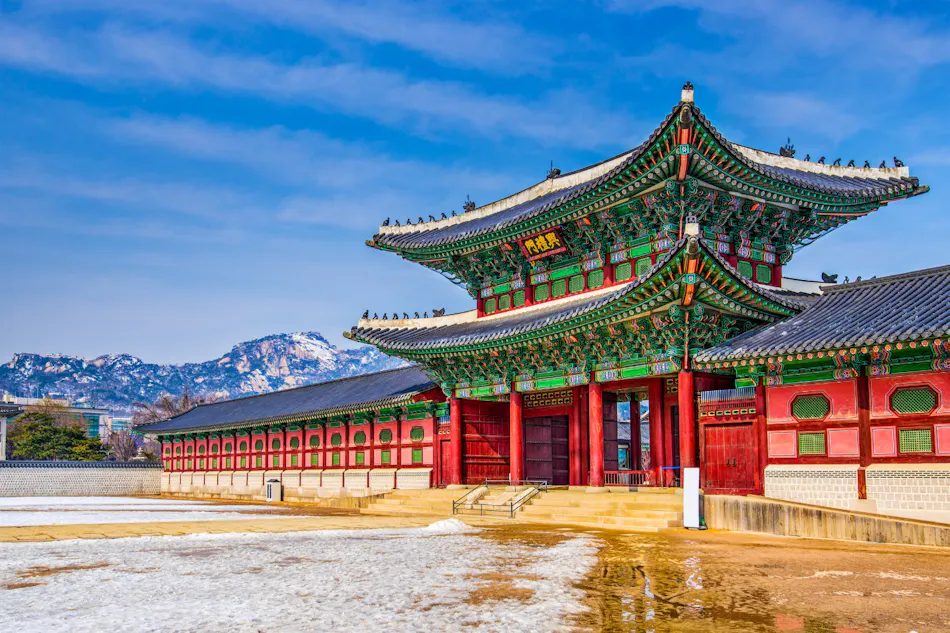 A vibrant Gyeongbokgung Palace in South Korea, featuring a snowy courtyard and majestic mountains.