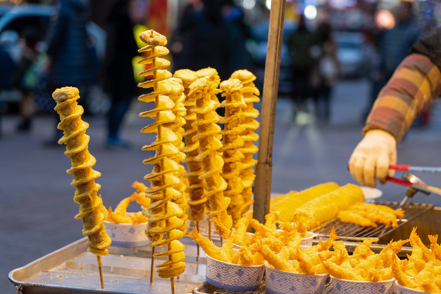 Golden spiral potatoes and fried shrimp on skewers at a vibrant South Korean street food market.