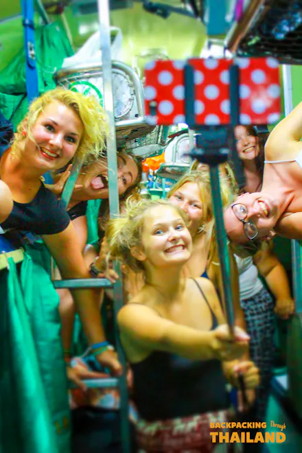 Happy young women take a selfie with a red polka dot stick on a lively Thailand night train.
