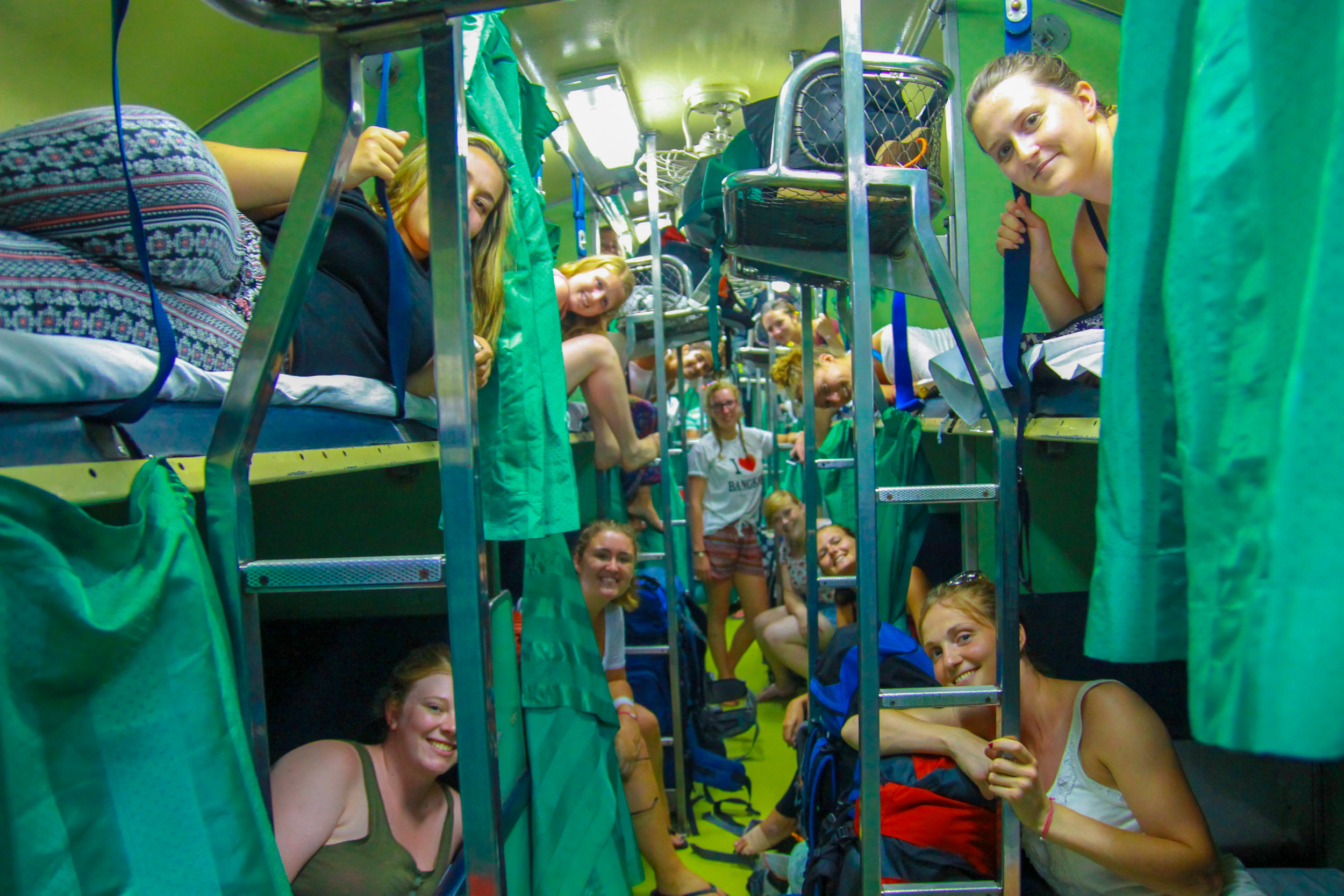 Happy backpackers socialize in bunk beds on a lively overnight train in Thailand.