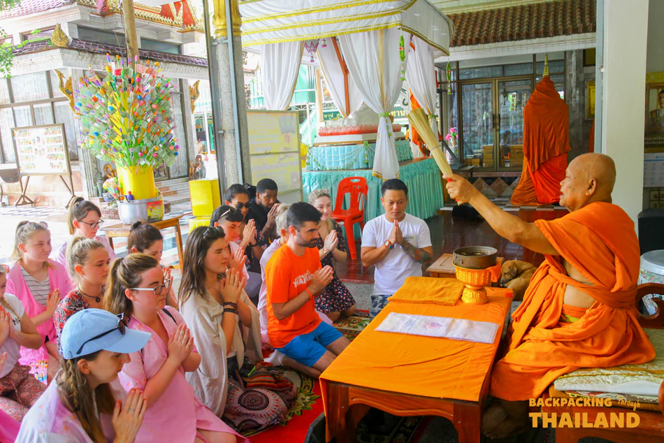 Travellers sitting on the temple floor as a Buddhist monk performs a blessing