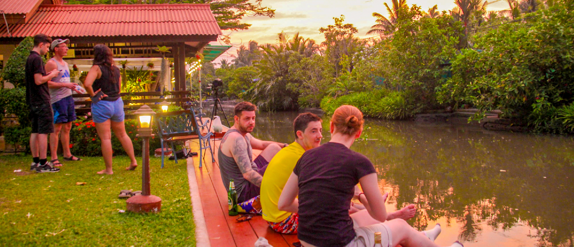 Tourists relax by a canal at sunset in Amaphawa, Thailand, enjoying the peaceful evening.