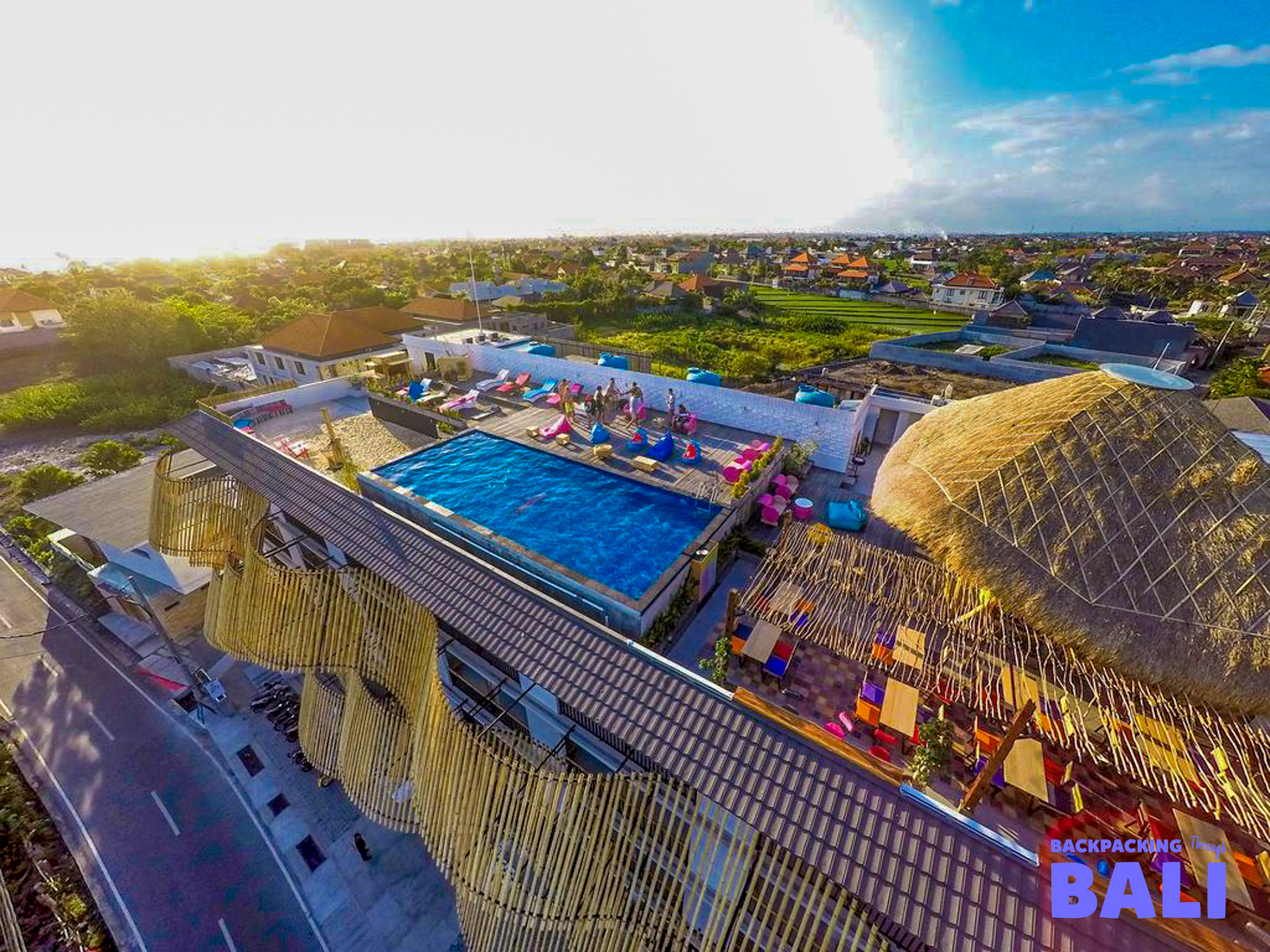 Relaxing rooftop pool with colorful lounge areas and a thatched bar overlooking Canggu, Bali.
