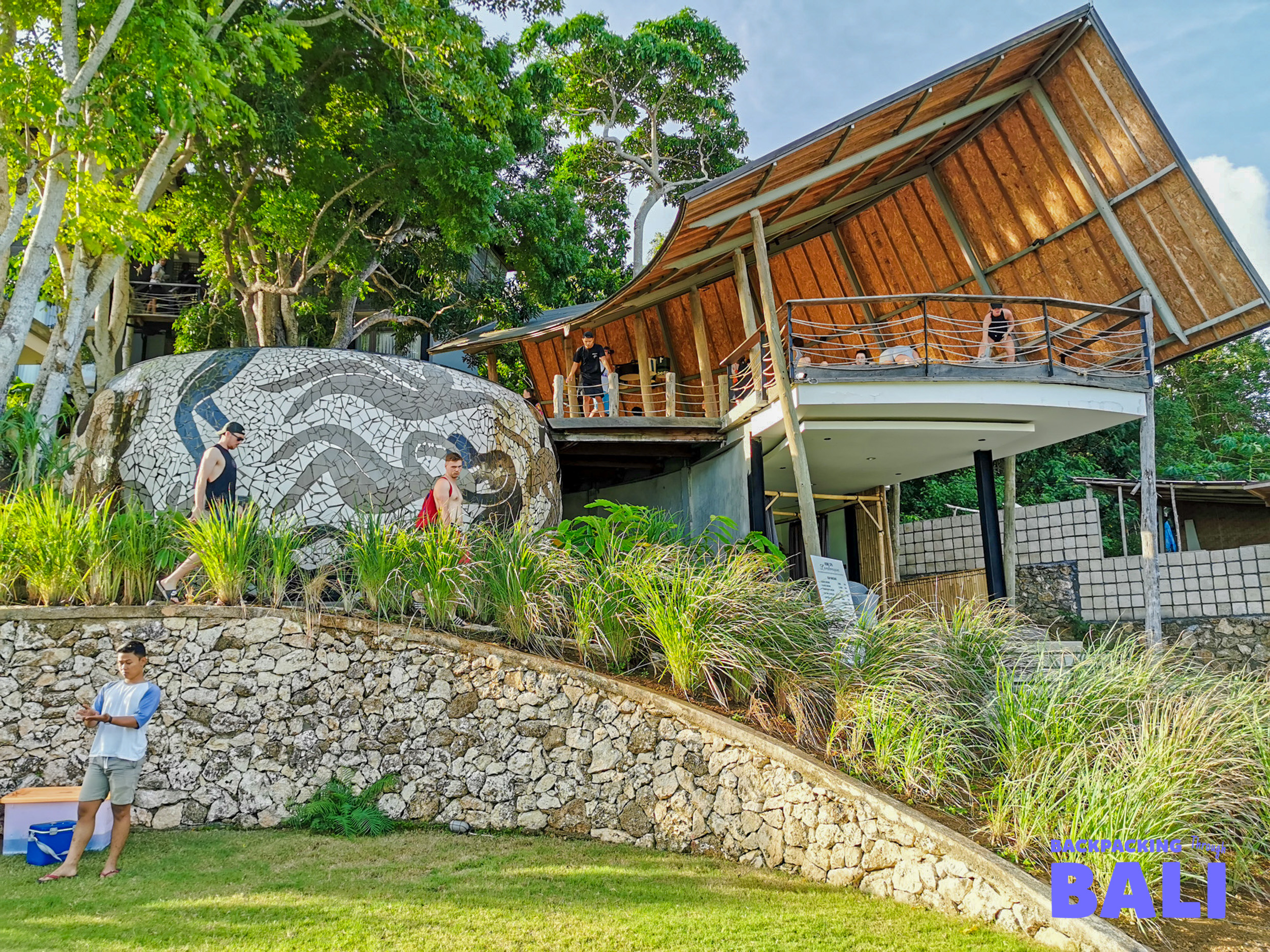 Travelers relax at a unique multi-level building with a curved thatched roof in Nusa Lembongan.