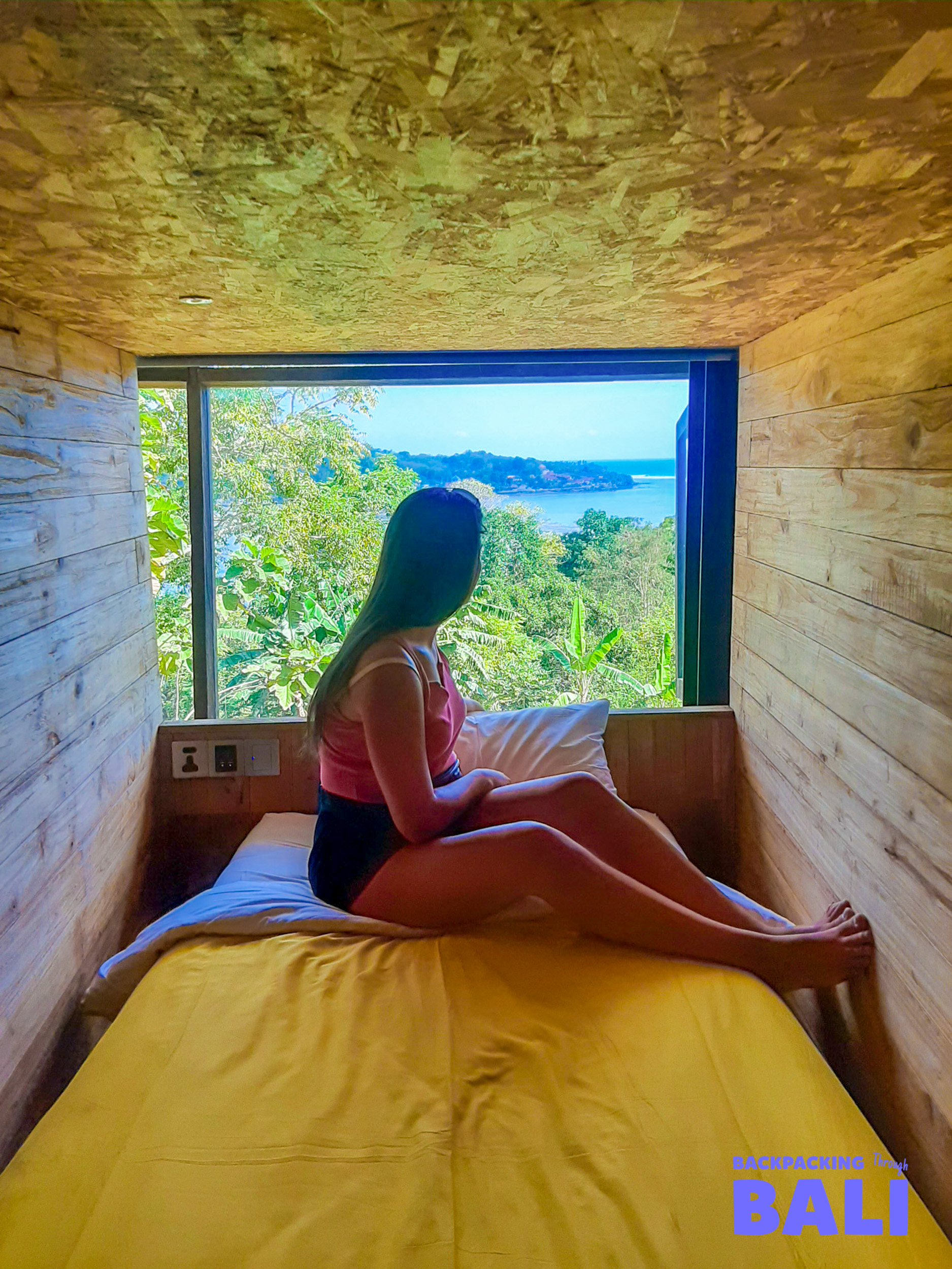 A traveler relaxes in a cozy wooden room, enjoying the beautiful island view of Nusa Lembongan.