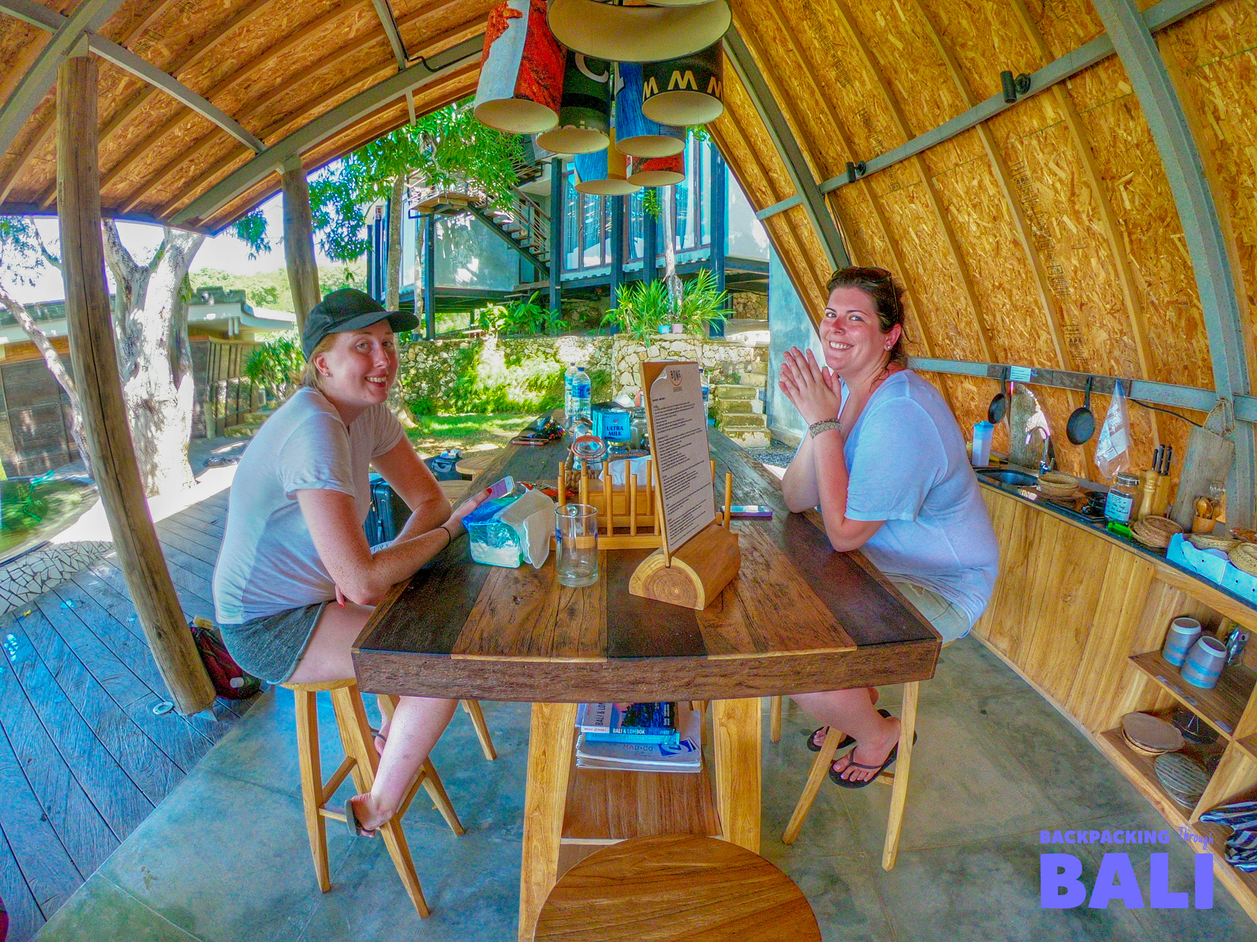 Two smiling women relaxing at a rustic open-air dining area in Nusa Lembongan, Bali.