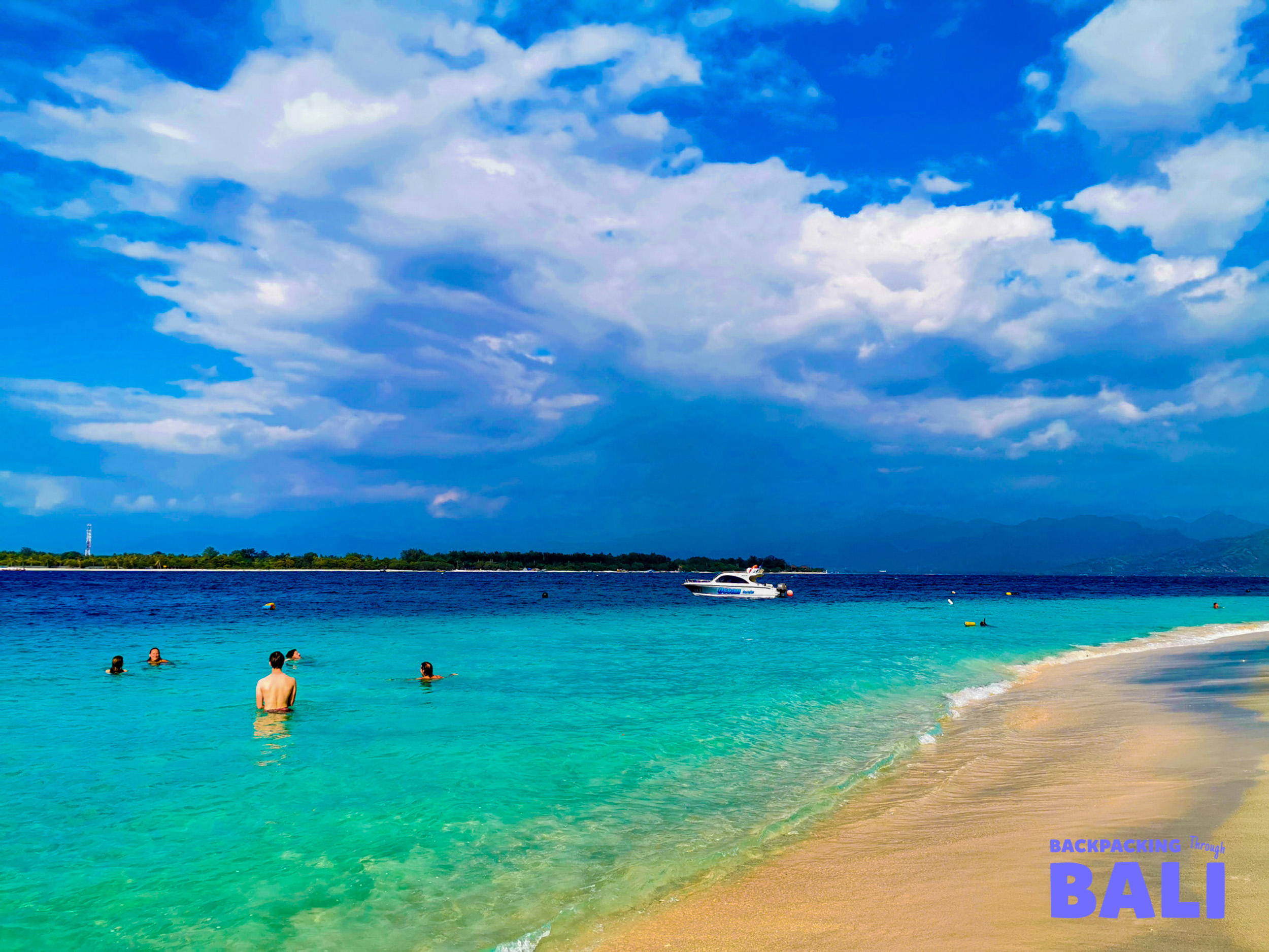 People swim in the clear turquoise waters of Gili Trawangan beach under a dramatic sky.
