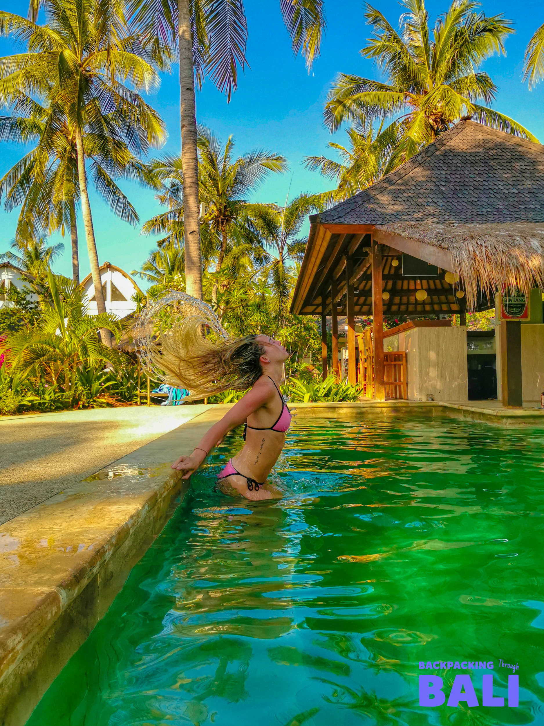 A woman in a pink bikini flips her wet hair in a tropical pool on Gili Trawangan.