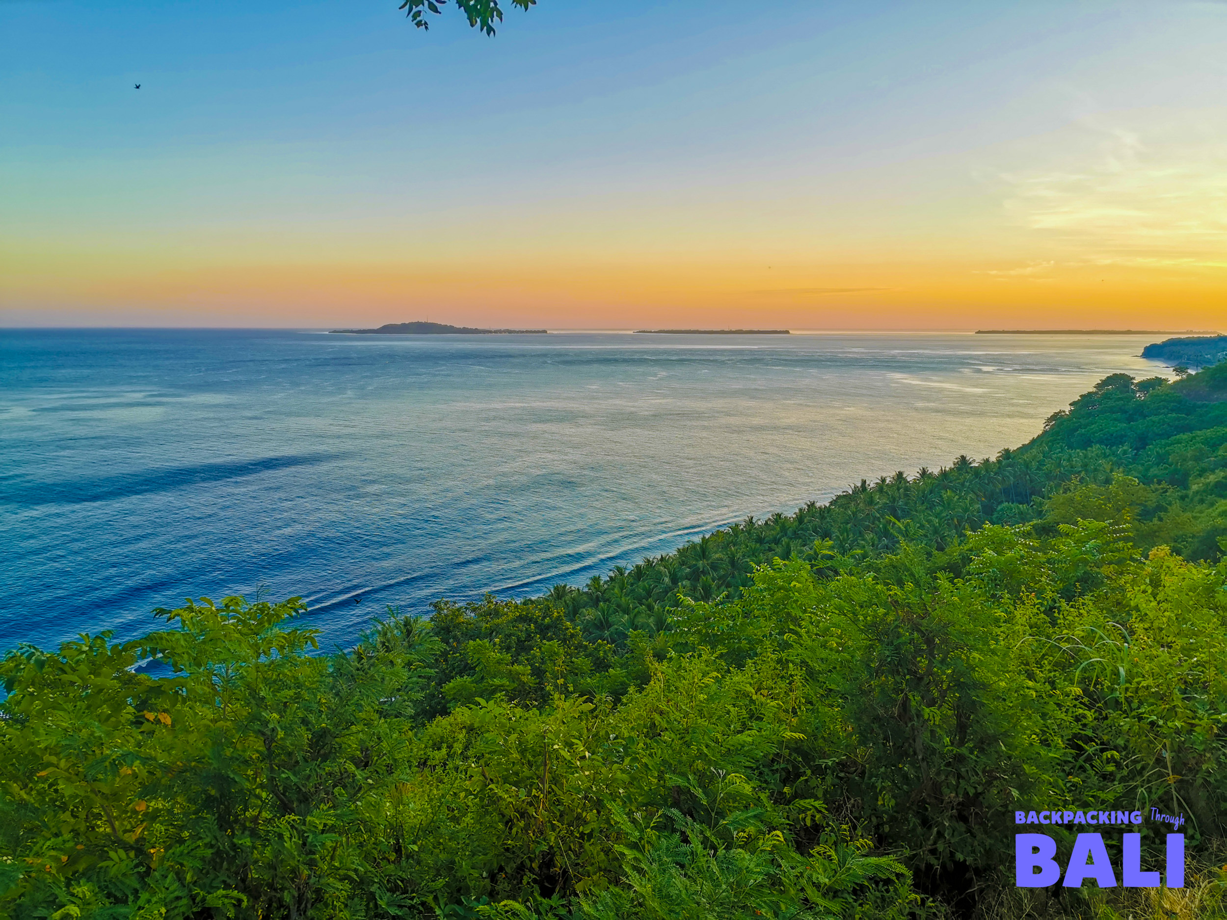Vibrant sunset colors paint the sky above the tranquil ocean and lush green hills of Gili Trawangan.