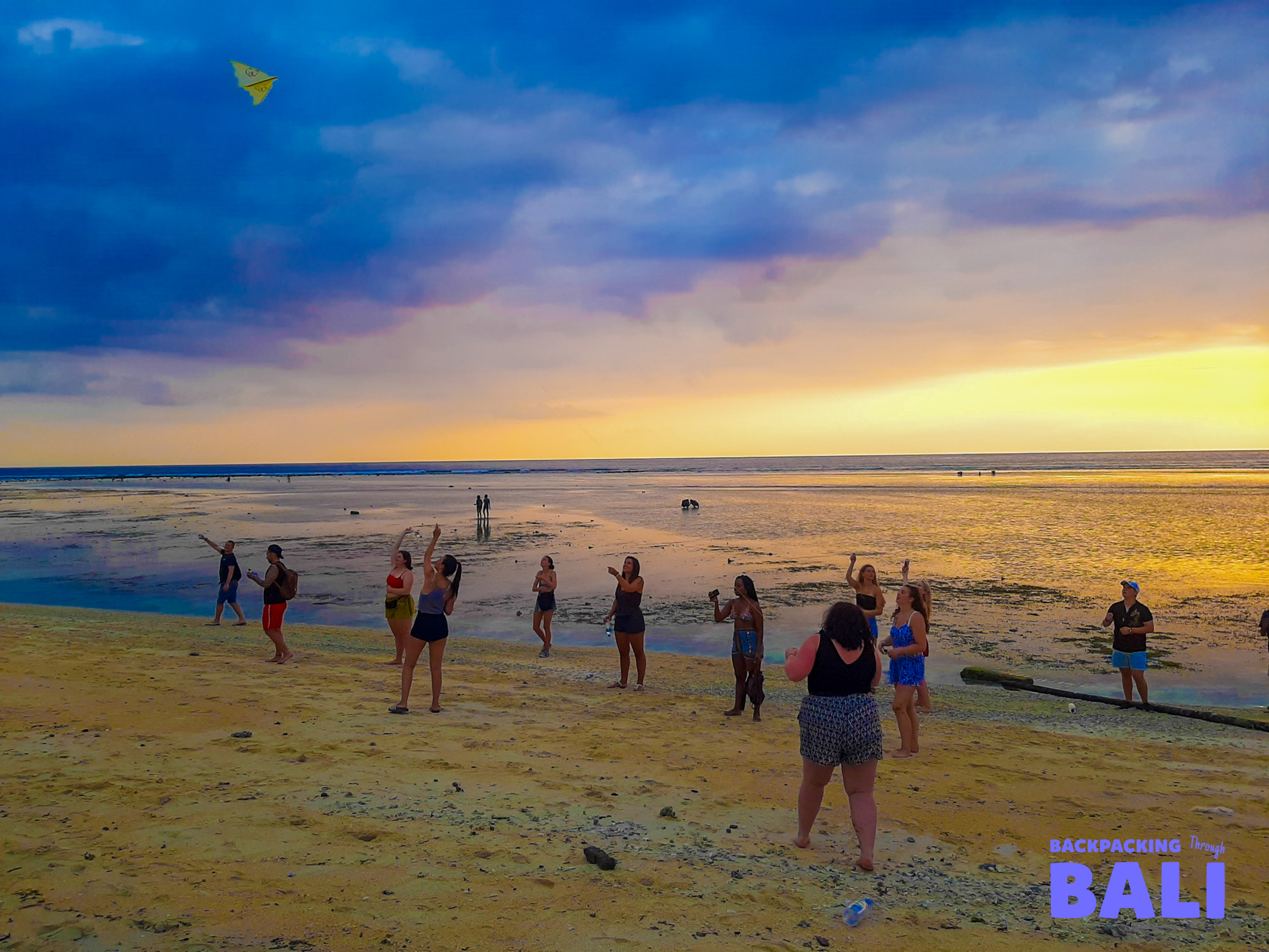 Friends flying kites on the wide sandy beach of Gili Trawangan during a vibrant sunset.
