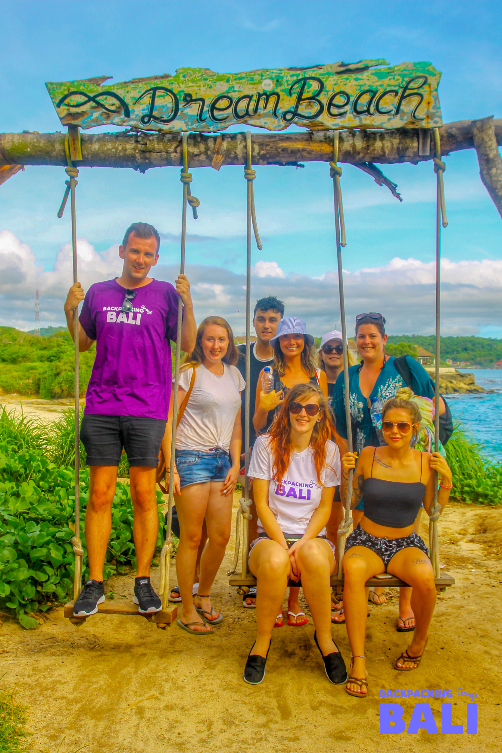 Backpackers pose happily on the iconic Dream Beach swing, enjoying the tropical vibes of Nusa Lembongan.