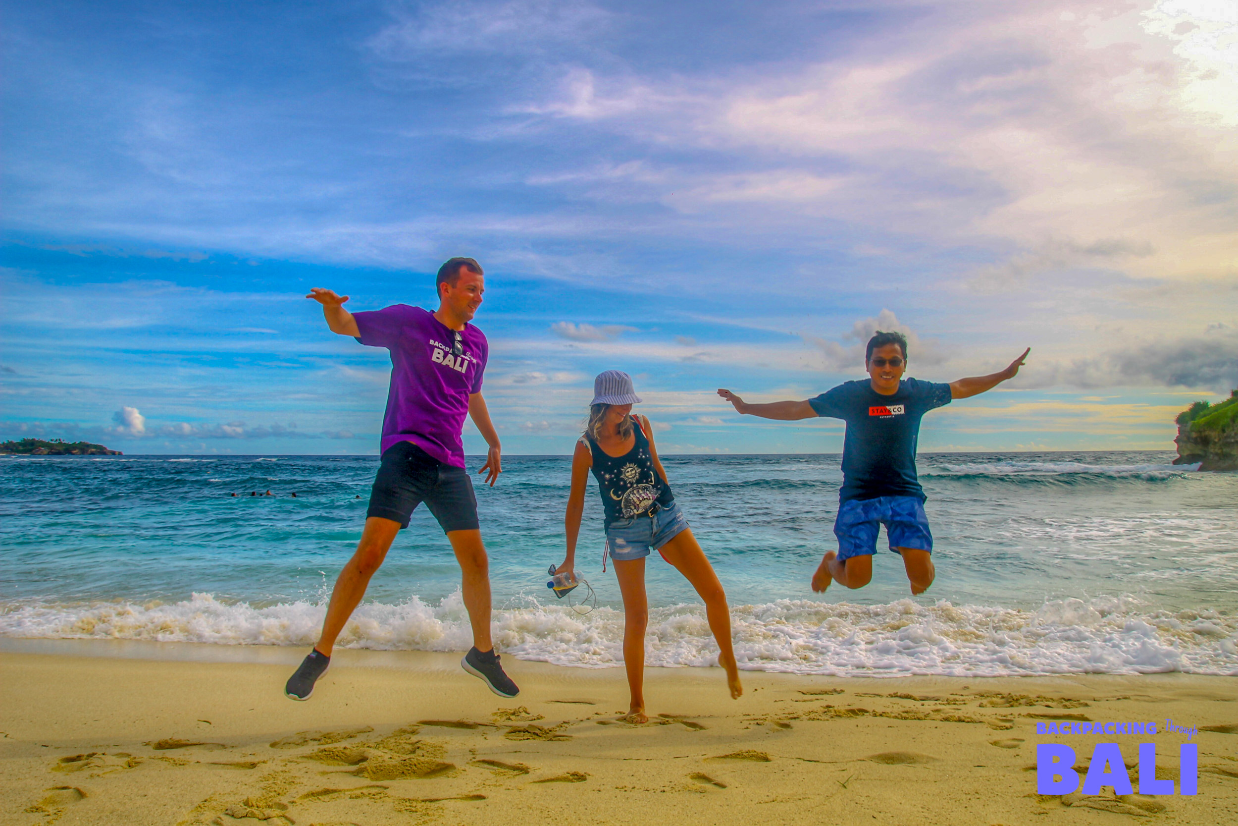 Three happy travelers jump for joy on a beautiful sandy beach in Nusa Lembongan, Bali.