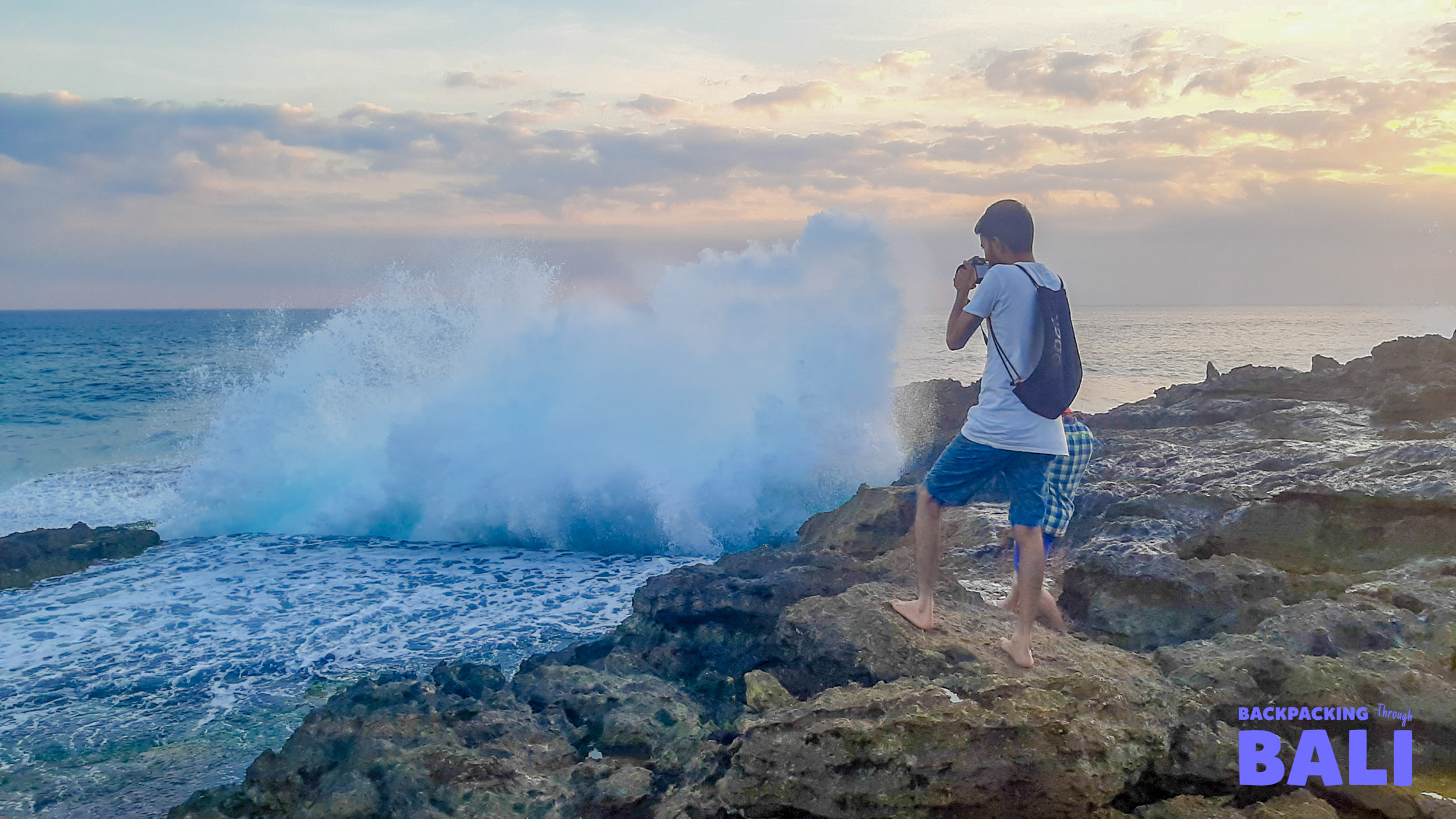 An adventurer captures a powerful ocean wave crashing against the rocky cliffs of Nusa Lembongan.
