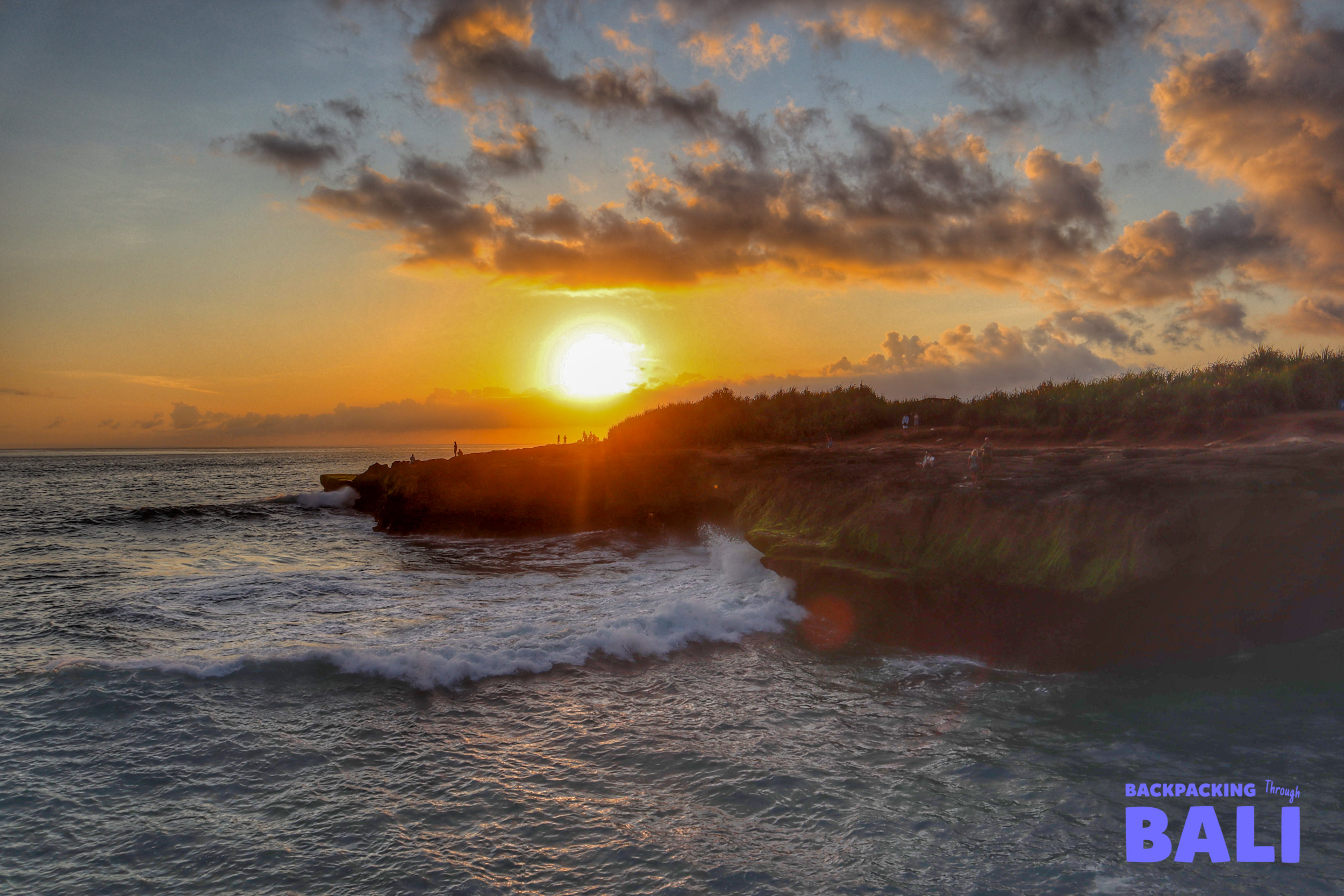 Vibrant sunset over the ocean at Devil's Tear, Nusa Lembongan, with waves on the rocky shore.