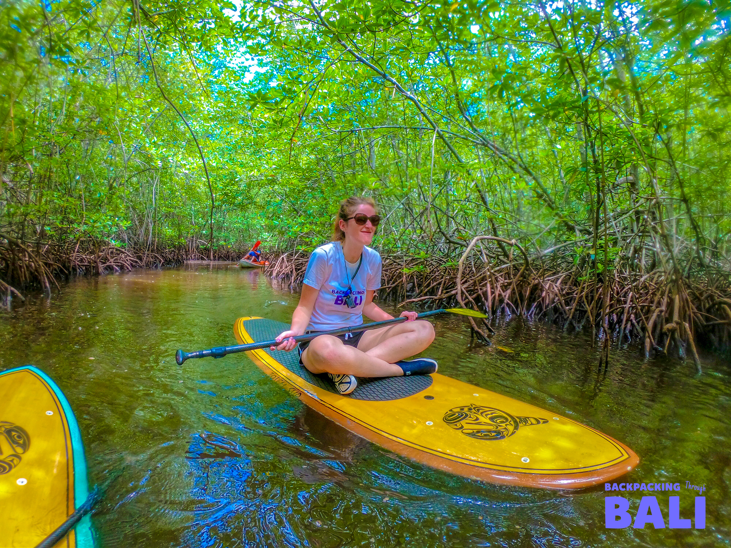 A woman paddleboarding through the calm mangrove forest waters of Nusa Lembongan, enjoying the chill island vibe.