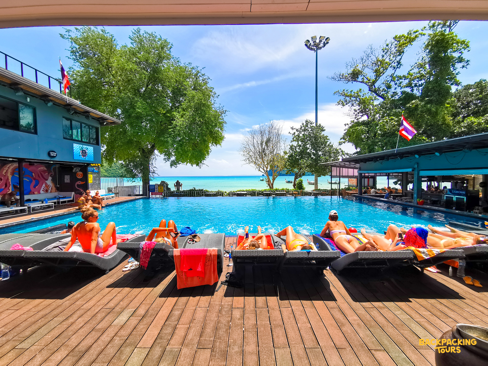 Sunbathers relax by a vibrant blue pool with a stunning ocean view at a Koh Phi Phi hostel.